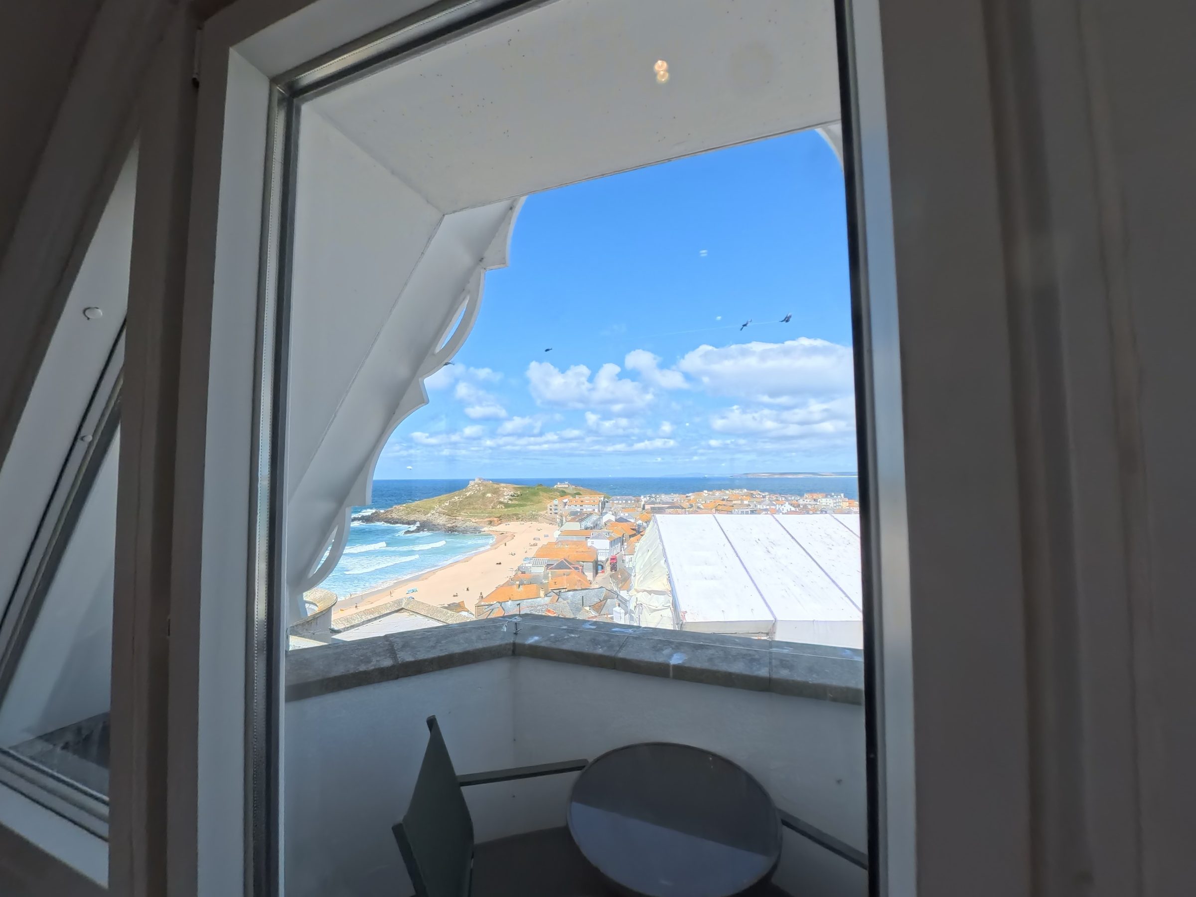 The balcony table and chairs at Tate Five, framed by the arched window, with St Ives beach and the sea beyond.