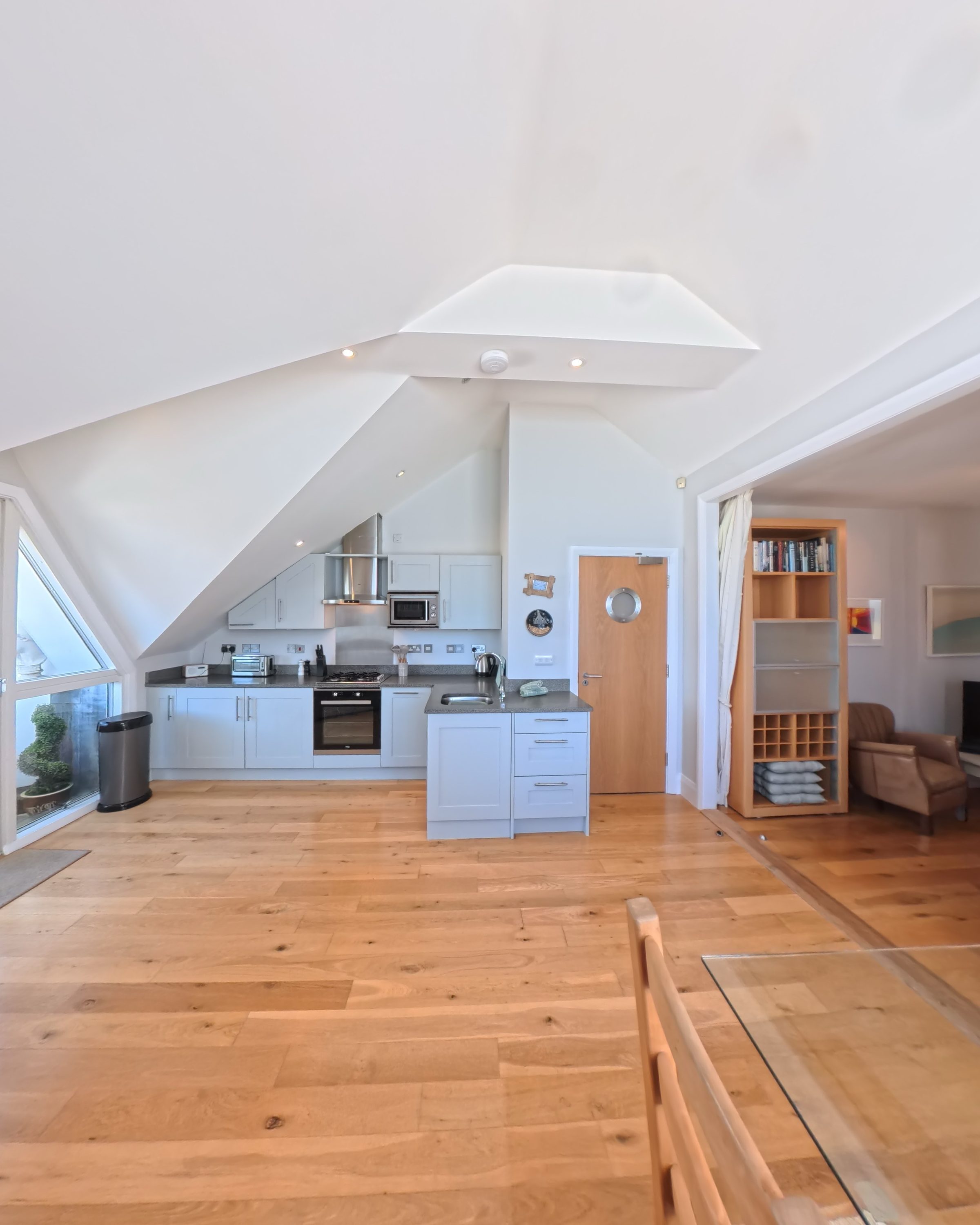 The vaulted living space at Tate Five, with raked dormer windows, the kitchen tucked under the eaves and the oak door with its porthole window.
