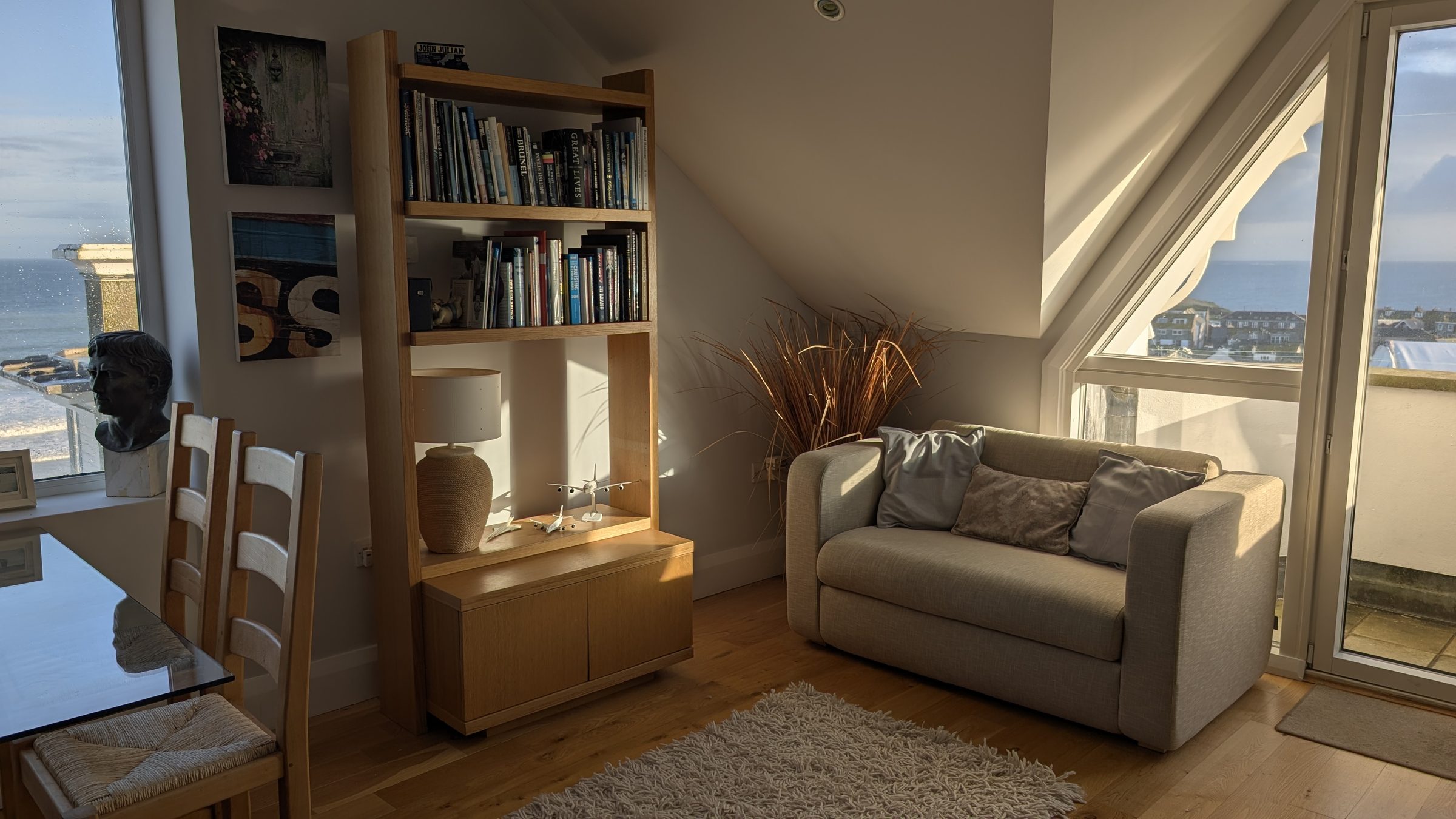 Late-afternoon sun on the oak floor at Tate Five, with the sofa, bookshelf and open balcony door.