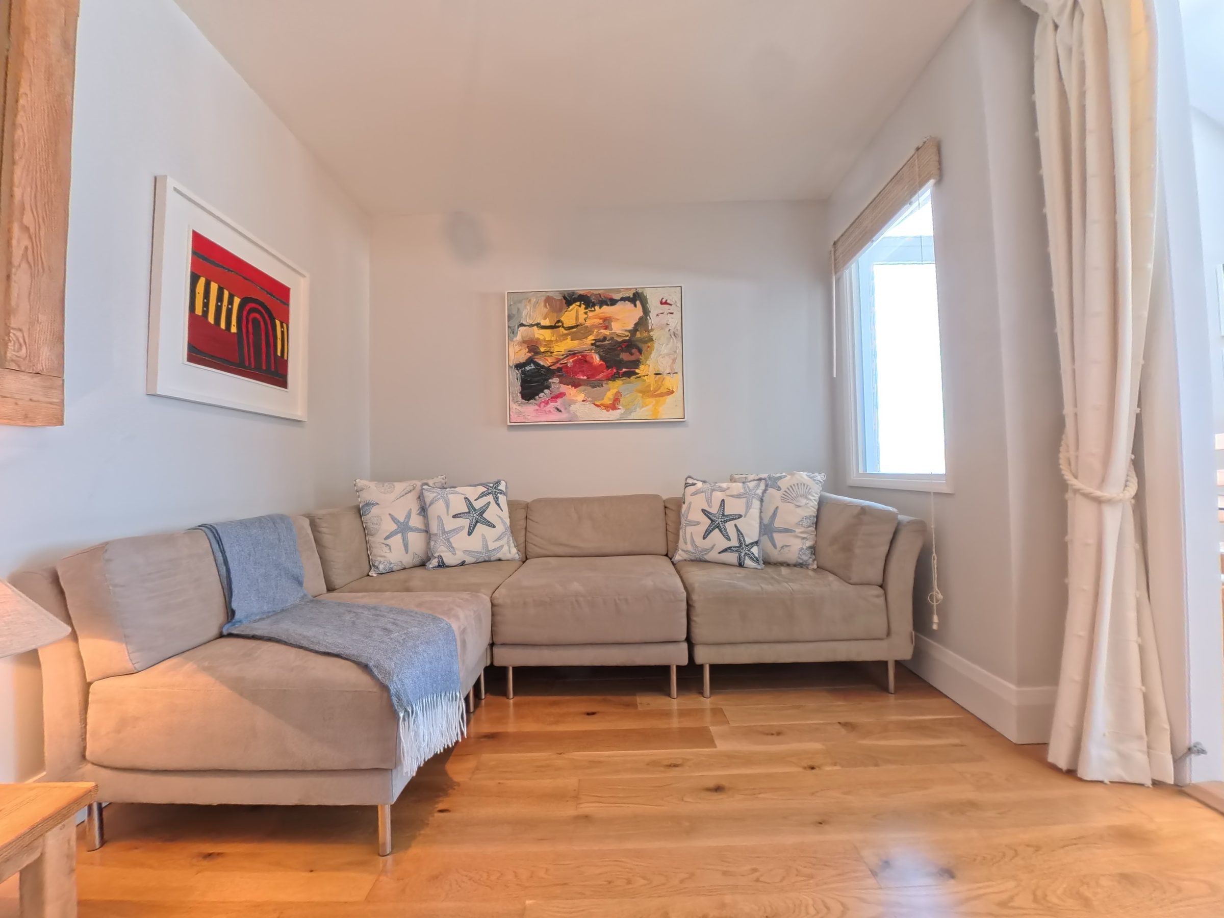 The snug at Tate Five, with a red, black and yellow abstract painting above the corner sofa, starfish cushions and a blue throw.